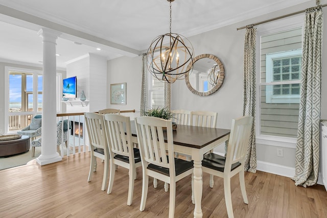 dining room featuring decorative columns, a fireplace, ornamental molding, light wood-style floors, and a chandelier