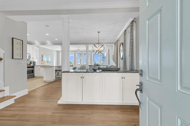 kitchen featuring ornate columns, a peninsula, stainless steel appliances, white cabinetry, and light wood-type flooring