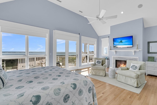 bedroom with a ceiling fan, wood finished floors, high vaulted ceiling, a premium fireplace, and access to exterior