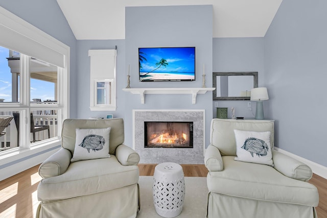 living area featuring baseboards, lofted ceiling, a lit fireplace, and wood finished floors