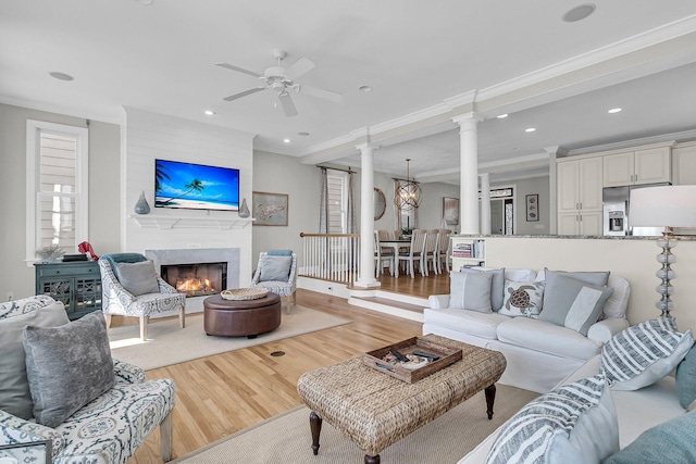 living area with wood finished floors, decorative columns, recessed lighting, a high end fireplace, and crown molding