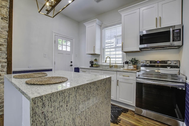 kitchen with stainless steel appliances, light stone countertops, a kitchen island, white cabinets, and sink