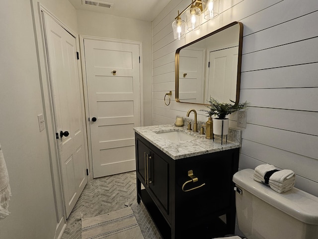 bathroom featuring vanity, wooden walls, and toilet