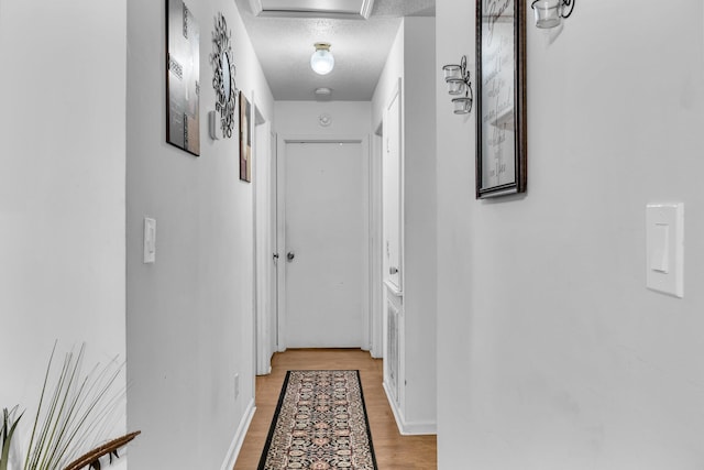 corridor with a textured ceiling and light wood-type flooring