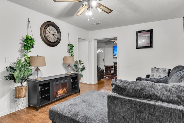 living room with hardwood / wood-style flooring, ceiling fan, and a textured ceiling