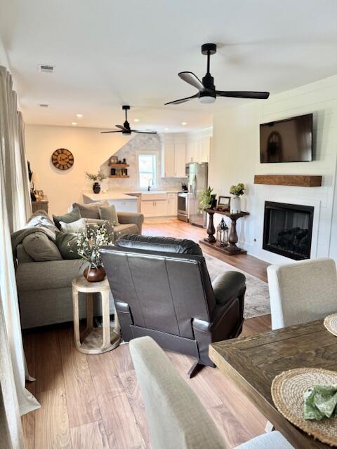living area with ceiling fan, light wood finished floors, a glass covered fireplace, and recessed lighting