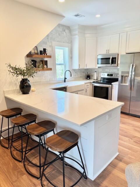 kitchen with appliances with stainless steel finishes, white cabinetry, a breakfast bar area, a peninsula, and a sink
