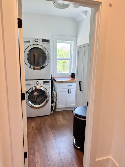 laundry area featuring stacked washer / dryer, hardwood / wood-style flooring, and cabinet space
