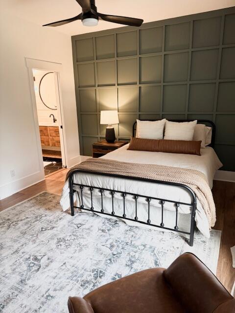 bedroom featuring baseboards, wood finished floors, ensuite bathroom, and a ceiling fan