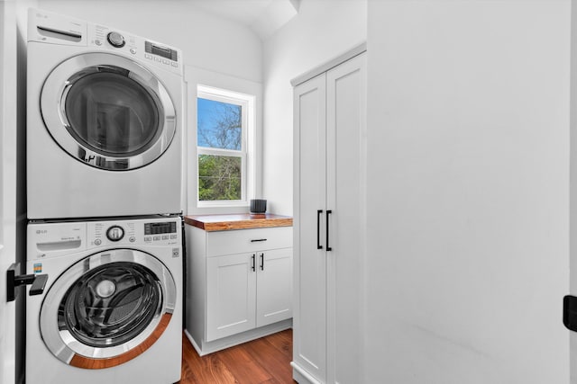 washroom featuring stacked washer and clothes dryer, cabinet space, and wood finished floors