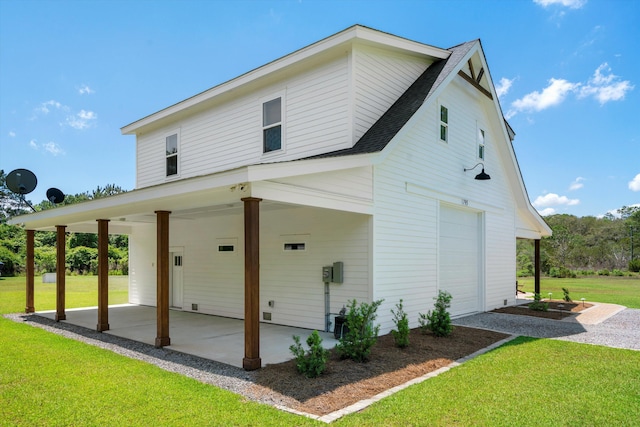 back of house featuring an attached garage, a yard, roof with shingles, a carport, and a patio