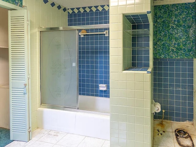 bathroom with tile walls, tile patterned floors, and shower / bath combination with glass door