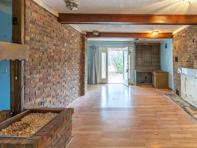 interior space featuring beam ceiling, a textured ceiling, brick wall, and light wood-type flooring