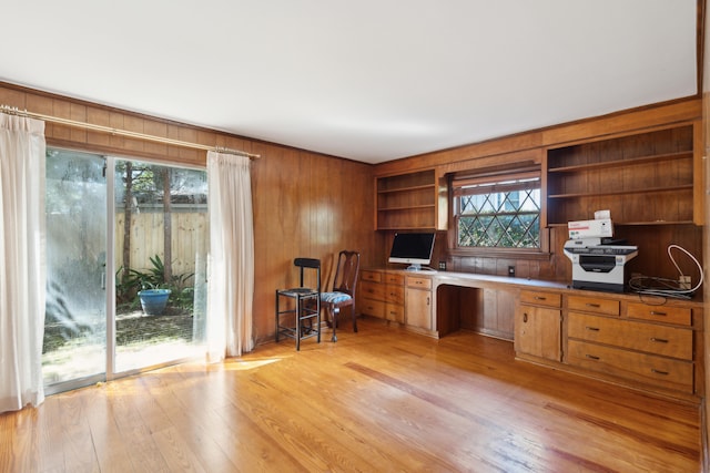 unfurnished office featuring light wood-type flooring, built in desk, built in features, and a healthy amount of sunlight