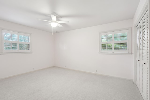 interior space featuring light carpet, multiple windows, ceiling fan, and a closet