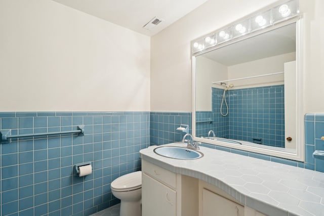 bathroom featuring tile walls, toilet, tiled shower, and vanity