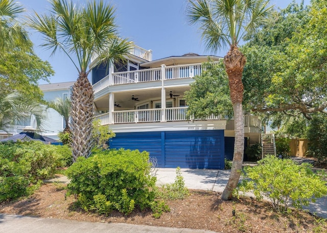 rear view of property with a garage, ceiling fan, a balcony, driveway, and stairs