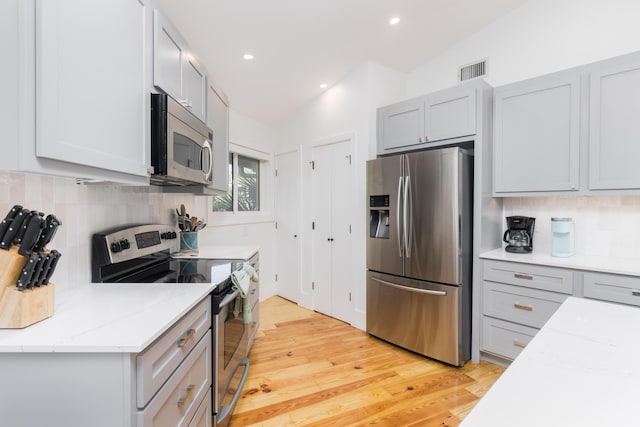 kitchen with stainless steel appliances, visible vents, light stone countertops, light wood-style floors, and decorative backsplash