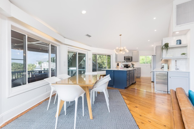 dining space with light wood-style floors, bar area, an inviting chandelier, and visible vents