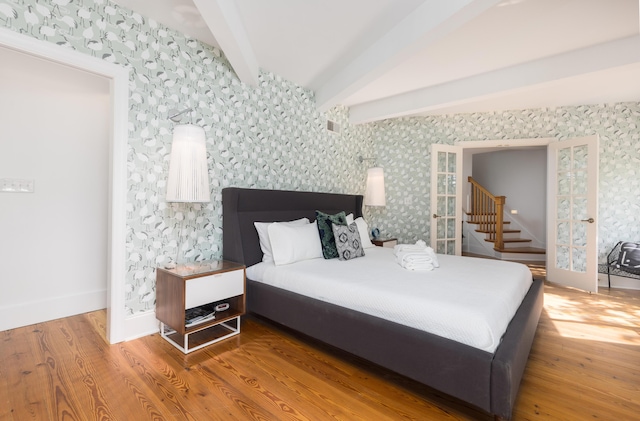 bedroom featuring visible vents, wallpapered walls, vaulted ceiling with beams, and wood finished floors