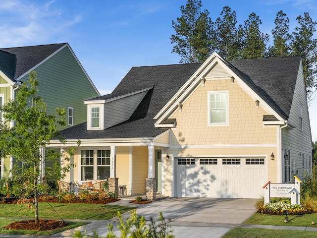 craftsman-style house with an attached garage, covered porch, a shingled roof, and concrete driveway