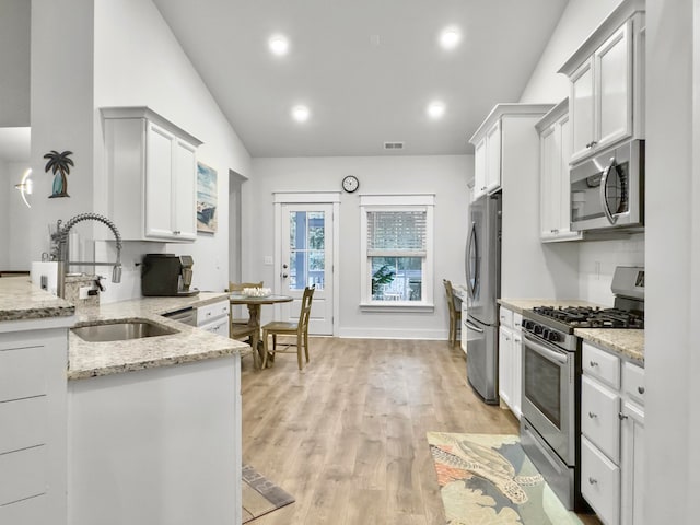 kitchen with white cabinets, lofted ceiling, light stone countertops, and appliances with stainless steel finishes