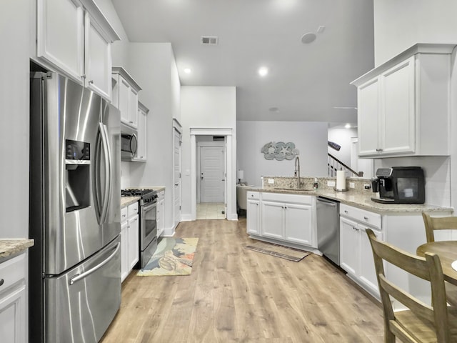 kitchen with light stone counters, stainless steel appliances, white cabinetry, light wood-type flooring, and sink