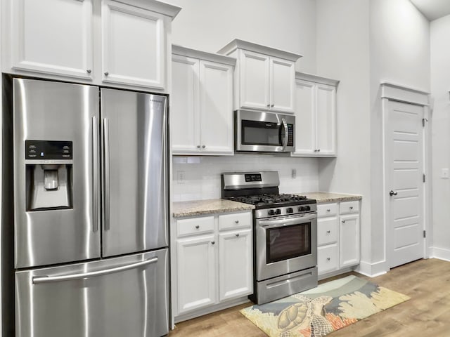 kitchen featuring tasteful backsplash, white cabinetry, appliances with stainless steel finishes, light stone countertops, and light hardwood / wood-style flooring