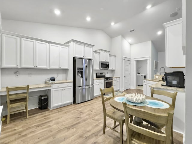 kitchen with light stone counters, white cabinetry, appliances with stainless steel finishes, light wood-type flooring, and lofted ceiling