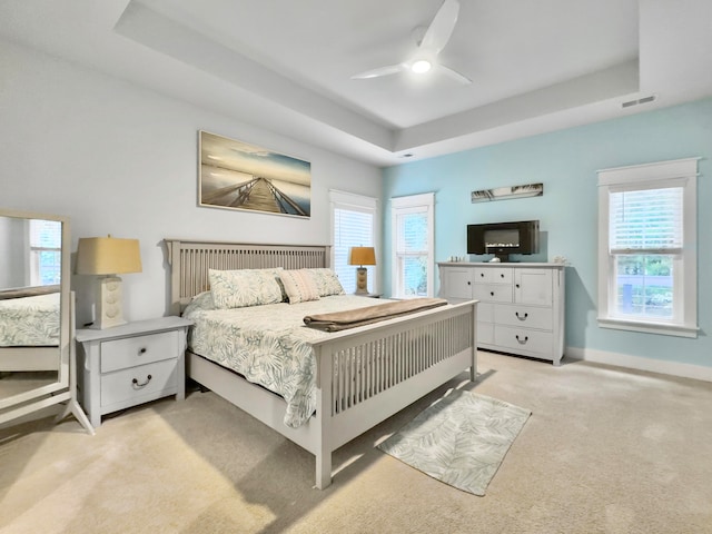 carpeted bedroom with ceiling fan and a tray ceiling