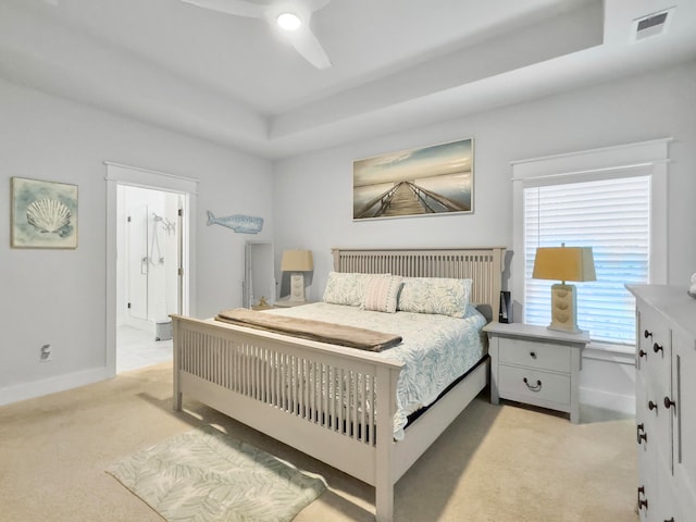 bedroom featuring a tray ceiling, light carpet, ceiling fan, and ensuite bath