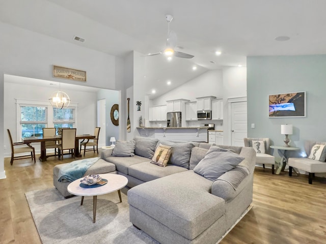 living room featuring light hardwood / wood-style floors, ceiling fan with notable chandelier, and high vaulted ceiling