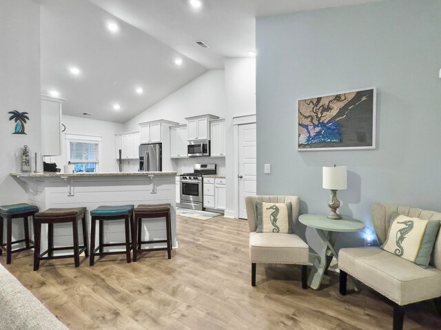 kitchen featuring white cabinetry, appliances with stainless steel finishes, a kitchen bar, light hardwood / wood-style floors, and kitchen peninsula