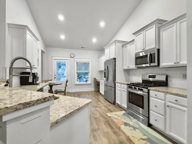 kitchen featuring stainless steel appliances, light stone counters, tasteful backsplash, light hardwood / wood-style flooring, and vaulted ceiling