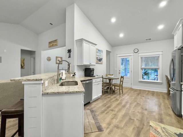 kitchen featuring stainless steel appliances, vaulted ceiling, kitchen peninsula, white cabinetry, and light hardwood / wood-style flooring