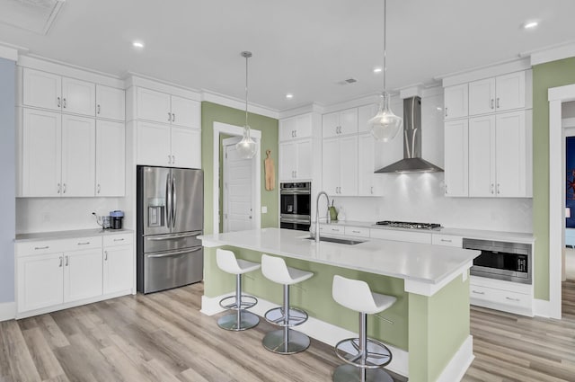 kitchen featuring pendant lighting, stainless steel appliances, light countertops, white cabinetry, and wall chimney range hood