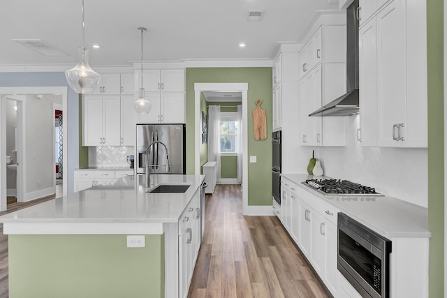 kitchen featuring a center island with sink, wall chimney exhaust hood, hanging light fixtures, stainless steel appliances, and light countertops