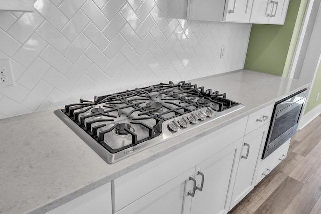 room details with light stone countertops, stainless steel gas cooktop, white cabinetry, light wood-type flooring, and decorative backsplash