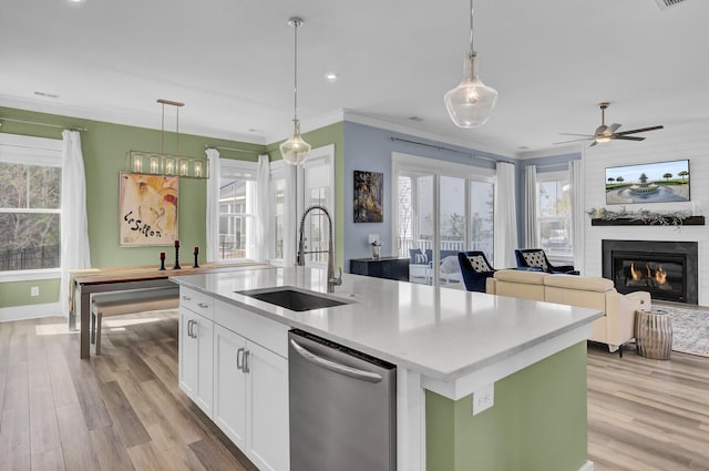 kitchen with a sink, white cabinetry, light countertops, hanging light fixtures, and a center island with sink