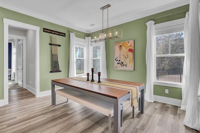 dining room with a notable chandelier, crown molding, light wood-style flooring, and baseboards