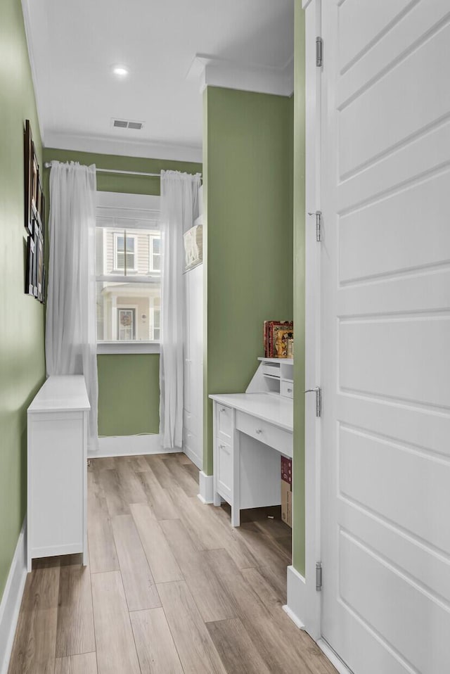 interior space featuring ornamental molding, light wood-type flooring, and baseboards