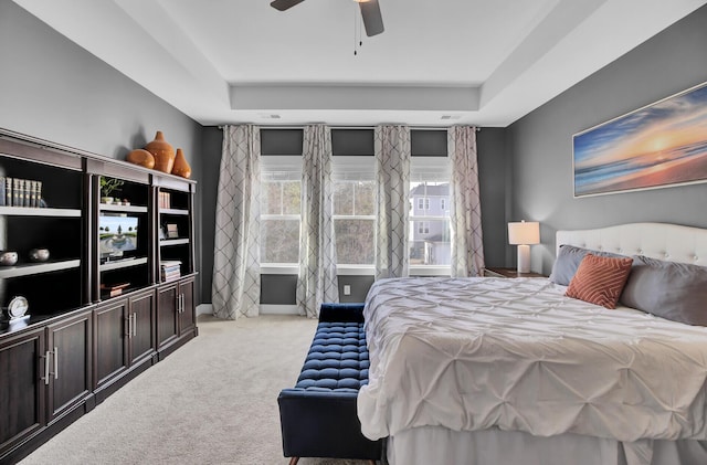 bedroom with a raised ceiling, a ceiling fan, and light colored carpet