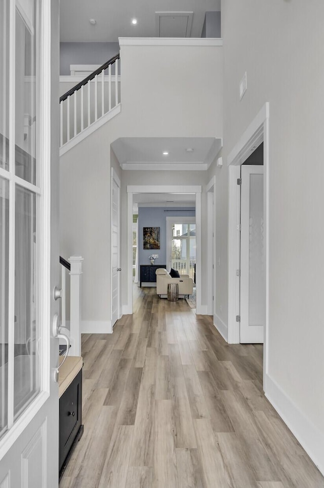 foyer with recessed lighting, light wood-type flooring, a towering ceiling, and baseboards