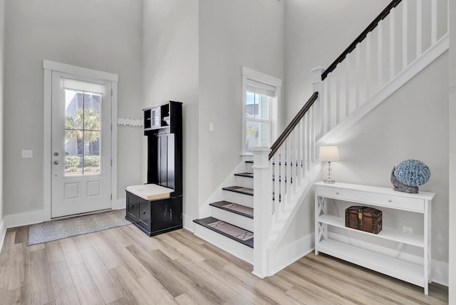 foyer featuring a towering ceiling, light wood-style floors, baseboards, and stairway