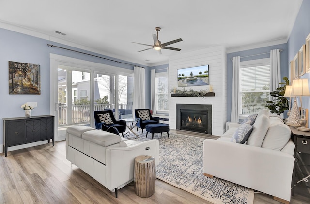living room featuring a large fireplace, a ceiling fan, visible vents, light wood-style floors, and crown molding
