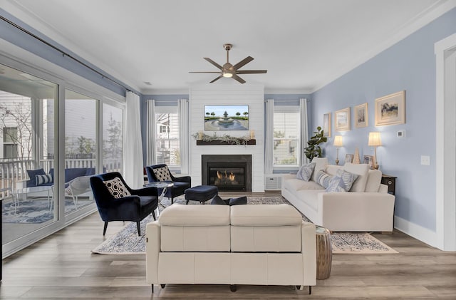 living area with a ceiling fan, light wood-type flooring, a large fireplace, and baseboards