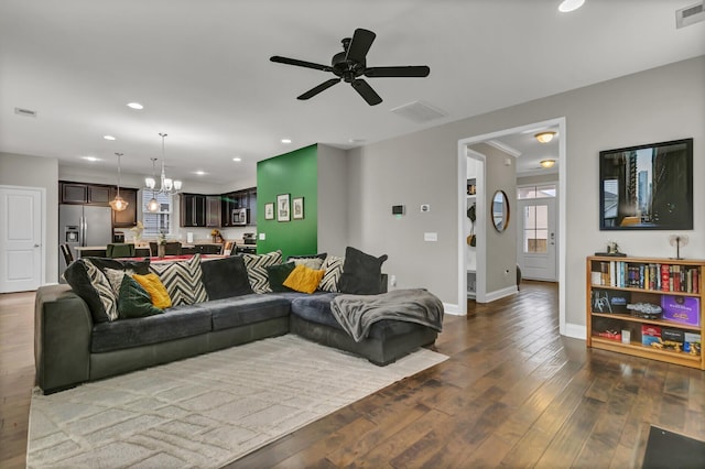 living room with ceiling fan with notable chandelier and dark hardwood / wood-style flooring