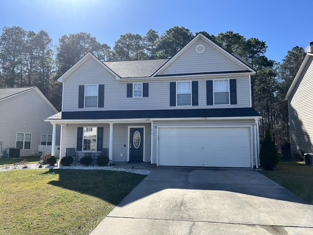 traditional-style home with driveway, a porch, a front yard, a garage, and central AC unit