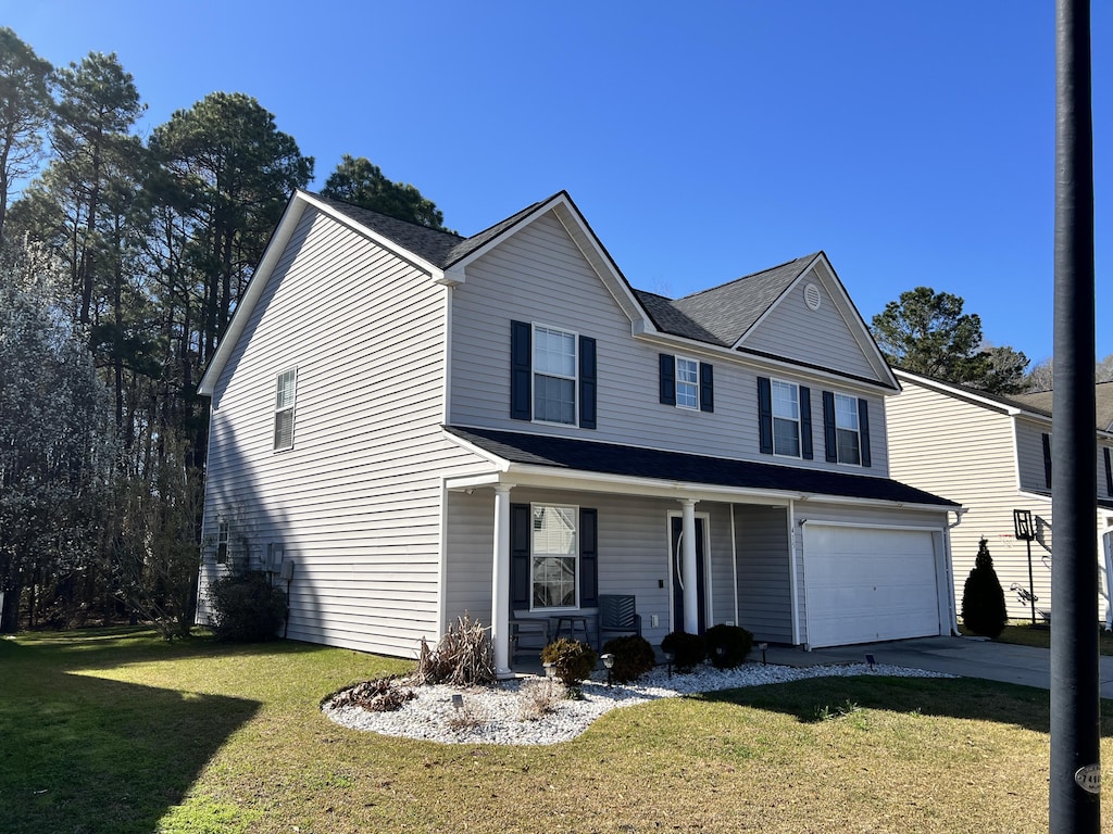 traditional home featuring a porch, an attached garage, a front lawn, and driveway