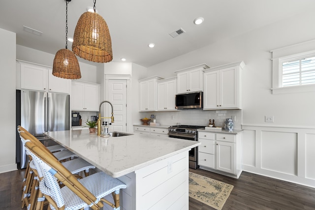 1713 Banning St, Mount Pleasant, SC 29466 - kitchen featuring appliances with stainless steel finishes, a kitchen island with sink, white cabinets, a kitchen bar, and a wainscoted wall